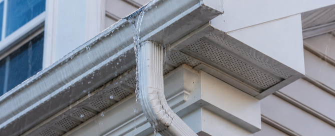 Eavestrough overflowing at a corner joint during rain, with soffit and fascia visible