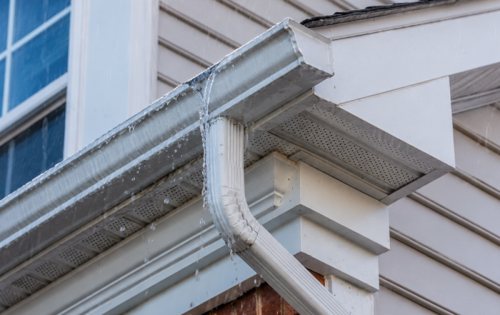 Eavestrough overflowing at a corner joint during rain, with soffit and fascia visible