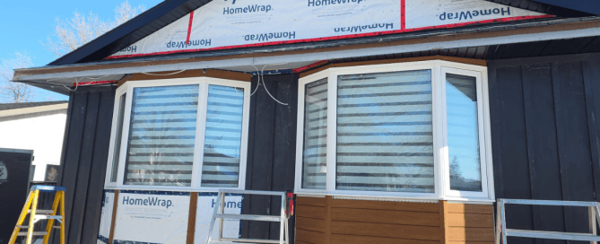 Residential siding contractor installing dark vertical siding over Tyvek HomeWrap weather barrier on a Winnipeg home.