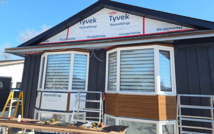 Residential siding contractor installing dark vertical siding over Tyvek HomeWrap weather barrier on a Winnipeg home.